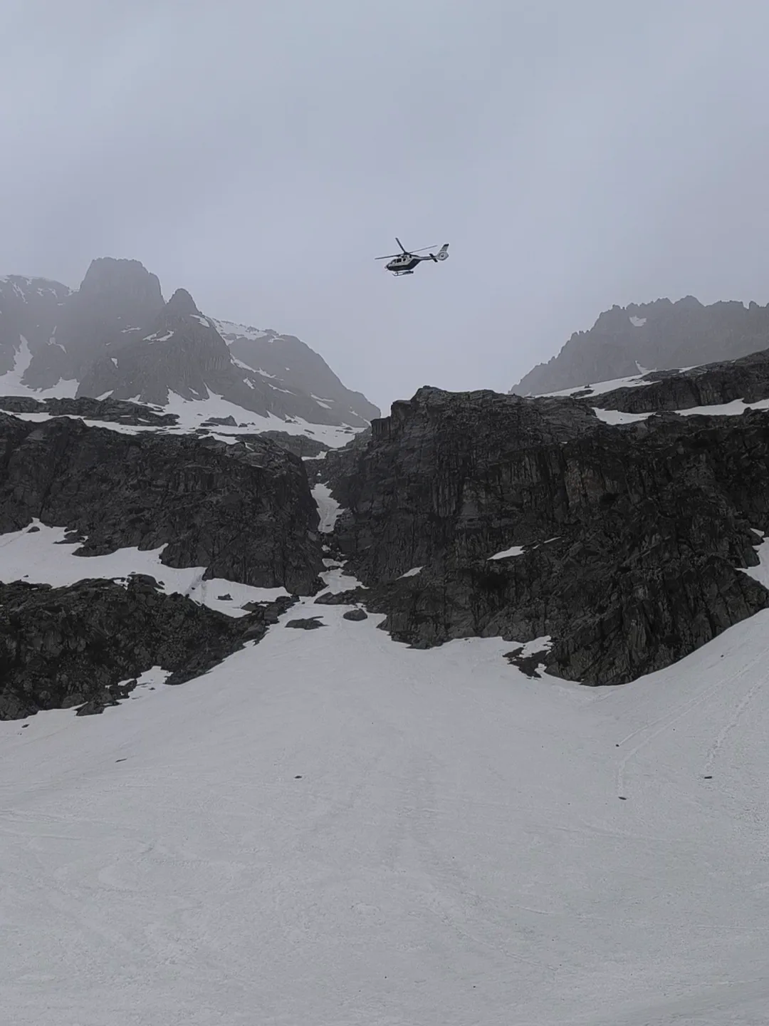 Helicóptero de rescate sobre un circo de montaña cubierto por nubes