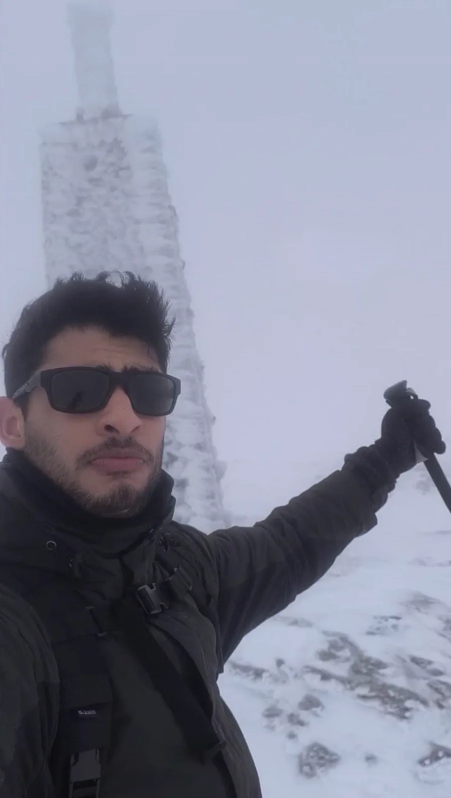 Autorretrato de Bauti junto al hito helado de cumbre entre la niebla