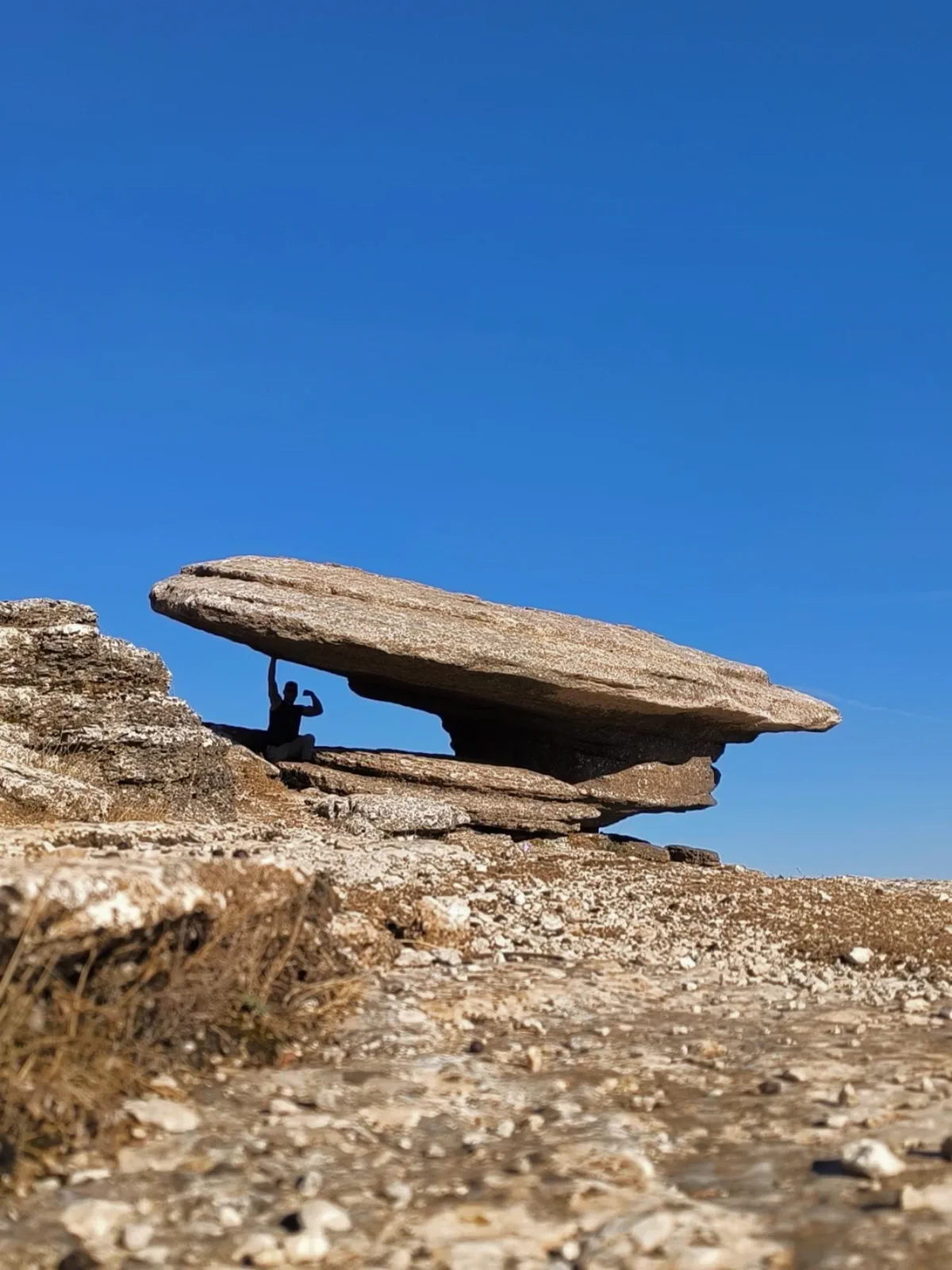 Gran roca plana aparentemente en equilibrio bajo el cielo azul